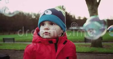 穿着红色夹克的小孩子在绿色公园前看着肥皂气球。 红色史诗4k相机。